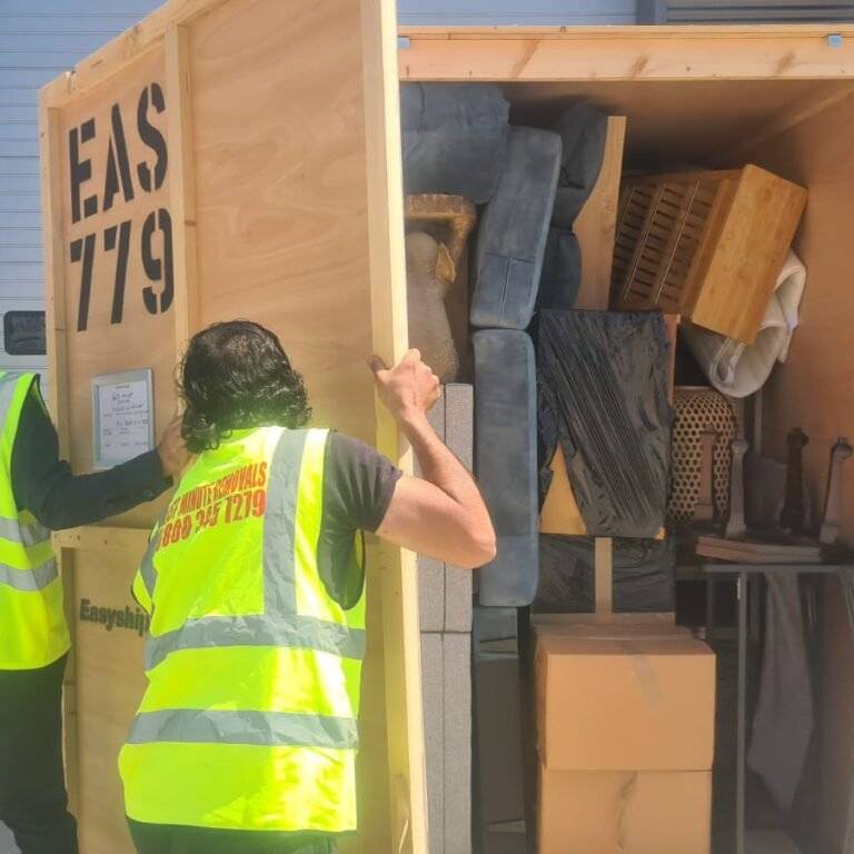 Movers in high-visibility vests securing a packed wooden storage crate filled with furniture and boxes – illustrating expert packing and storage services.