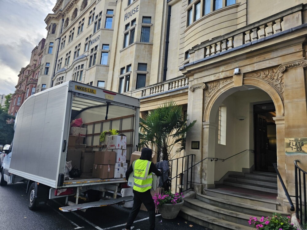 Professional movers unloading boxes from a moving van outside a large residential building during relocation.