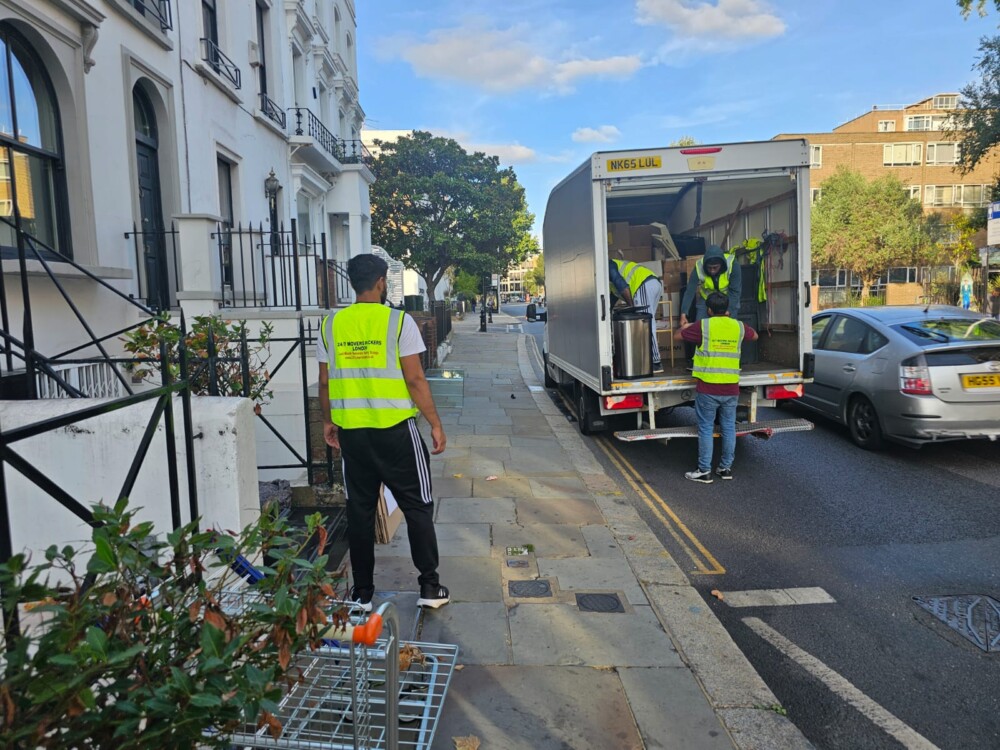 Team of movers in high-visibility vests loading household items and boxes into a moving van on a city street.