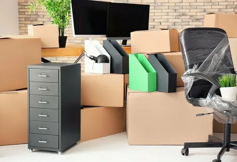 Packed office with moving boxes, wrapped office chair, file organizers, and drawer unit ready for relocation.